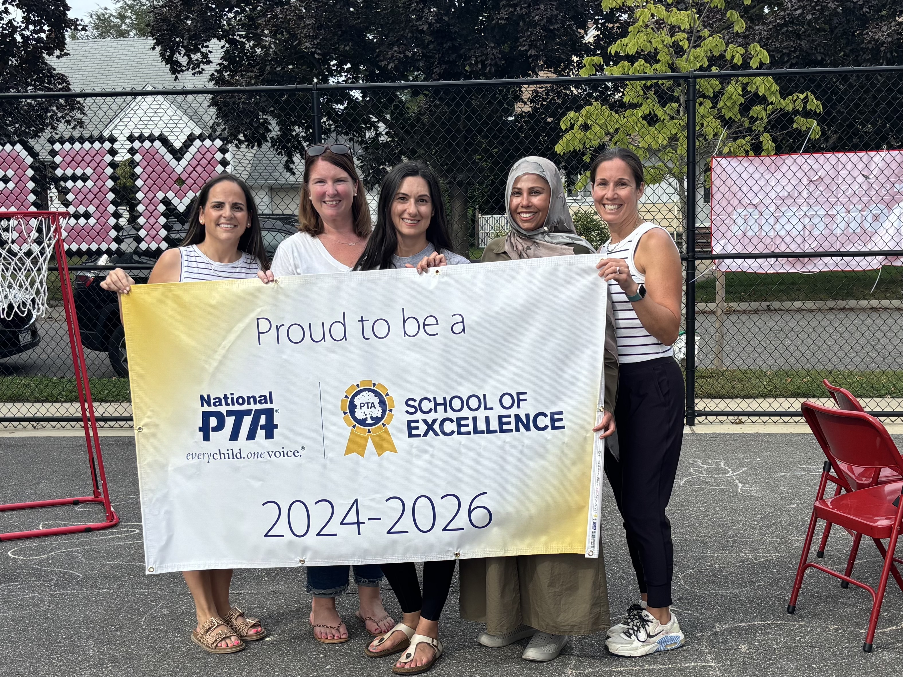 Five women smiling holding a school of excellence banner on a playground